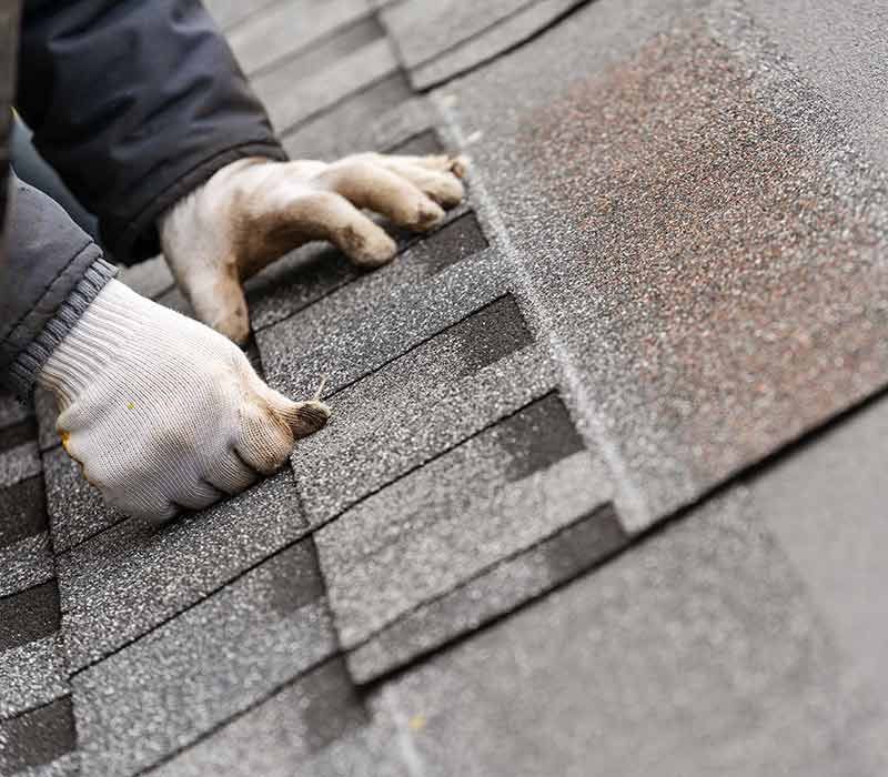 Close up of a worker with gloves putting down gray shingles on a residential roof