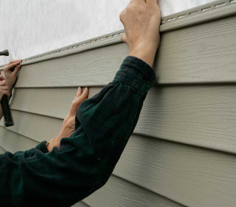 Close up of workers putting up green vinyl siding on a residential home